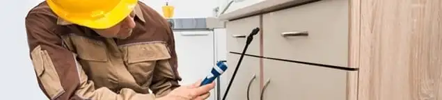 Roach exterminator applying treatment under kitchen cabinets in Staten Island, NY